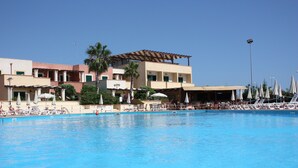 A swimming pool area with lounge chairs and umbrellas, a covered seating area, and a multi-story building with balconies. - L'Arco del Saracino (Salve)