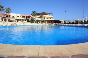 A large swimming pool with lounge chairs and umbrellas, surrounded by buildings with palm trees and a clear sky. - L'Arco del Saracino (Salve)