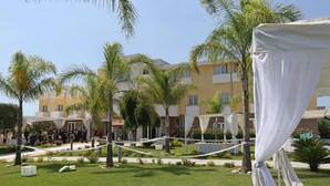 A courtyard with a white canopy, palm trees, and a building with balconies. - Medea Resort (Bellona)