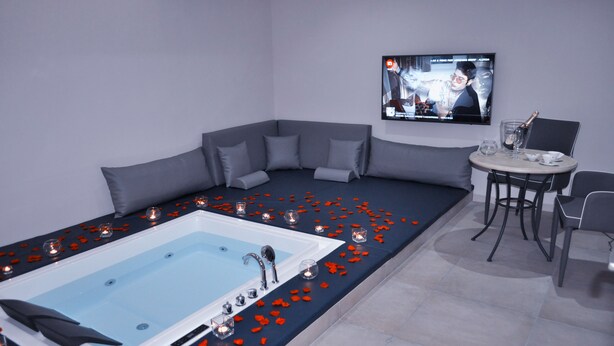 A modern bathroom with a large bathtub, a small table with a glass of champagne, and a television mounted on the wall. - Medea Resort (Bellona)