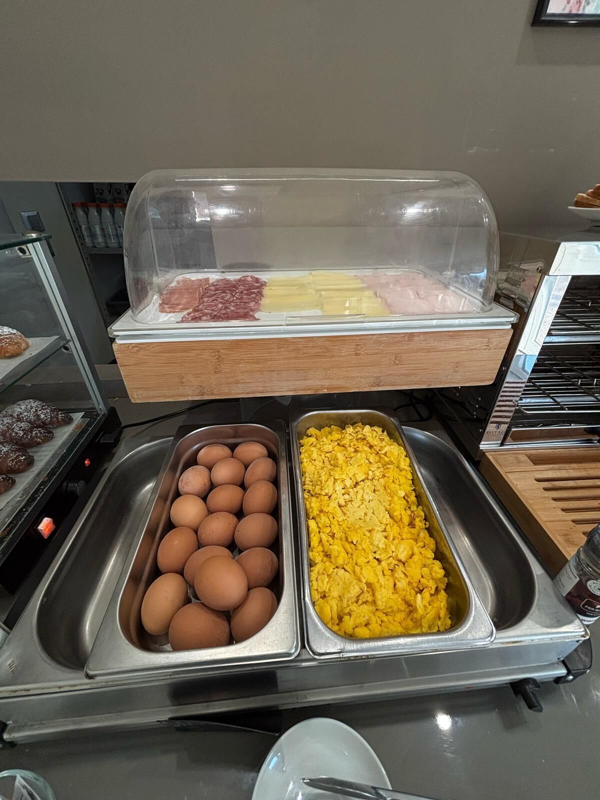 A breakfast buffet with trays of eggs, scrambled eggs, and various meats.