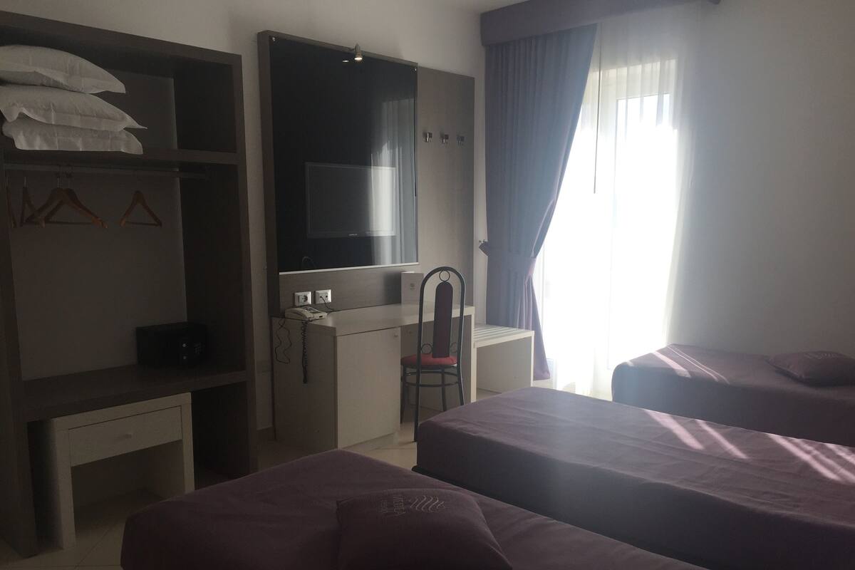 A hotel room with two beds, a desk with a chair, a wardrobe, and a large mirror.