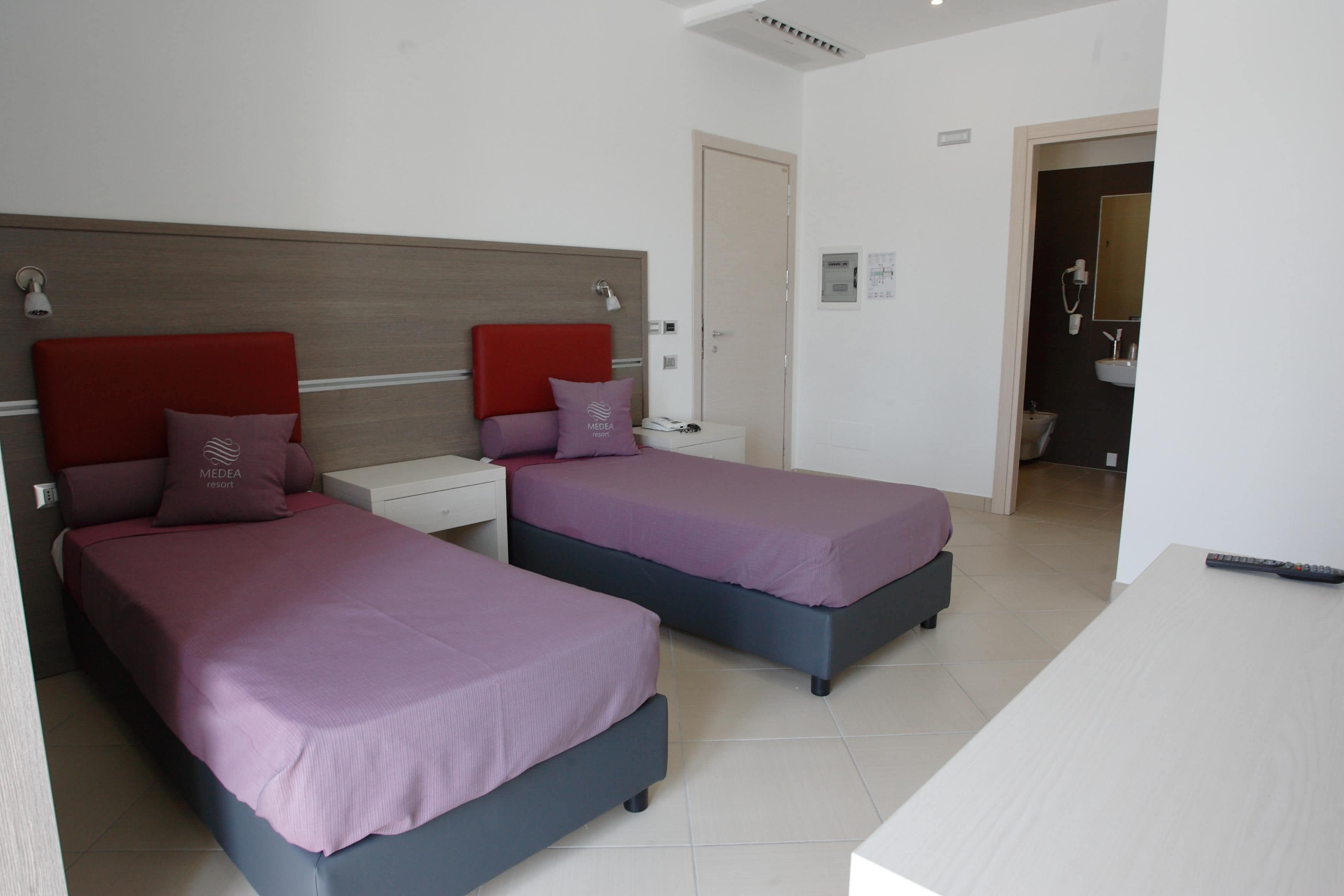 Une chambre d’hôtel avec deux lits, un bureau et une salle de bain visible à travers une porte ouverte.