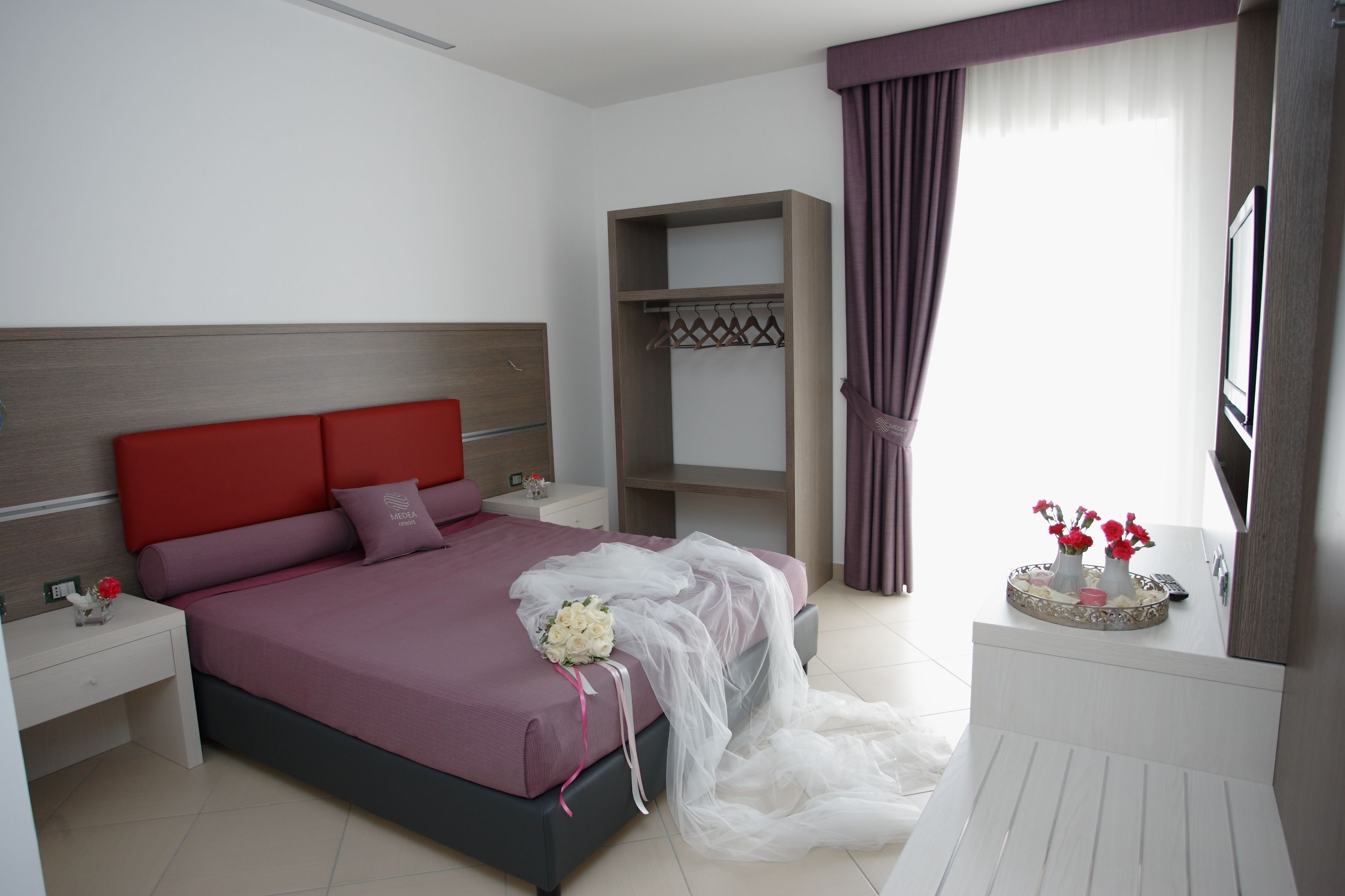Un dormitorio moderno con un cabecero rojo, una cama grande, un armario y un tocador con espejo.