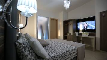 A modern bedroom with a bed, bedside lamp, and a TV on a desk.
