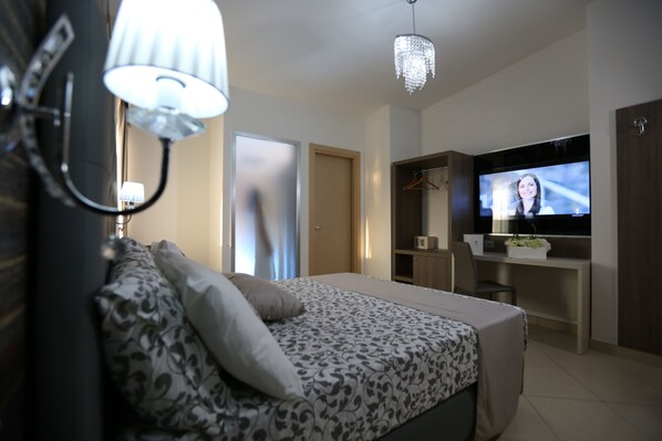 A modern bedroom with a bed, bedside lamp, and a TV on a desk.