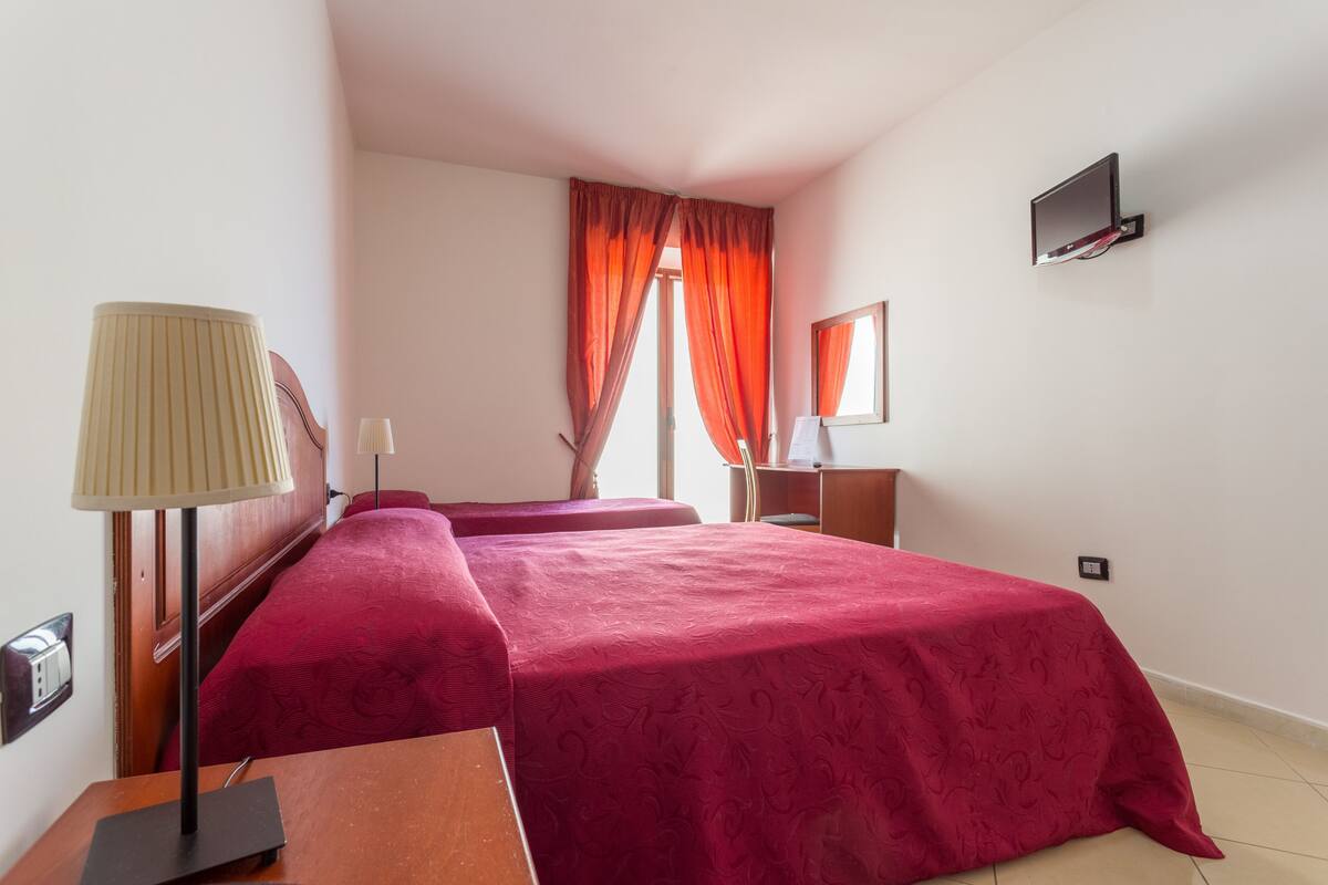 A hotel room with two beds, a desk, a lamp, a mirror, and a TV mounted on the wall.