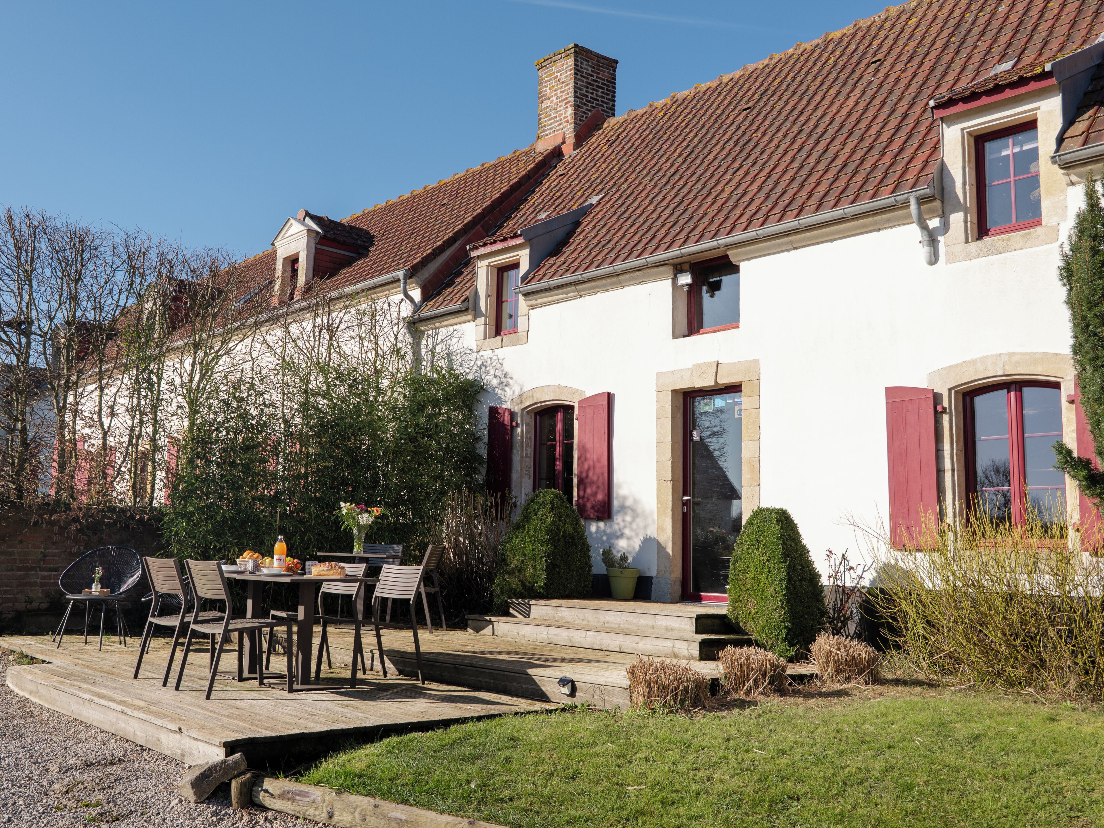 A two-story house with a tiled roof, a front porch with a table and chairs, and a small garden area.
