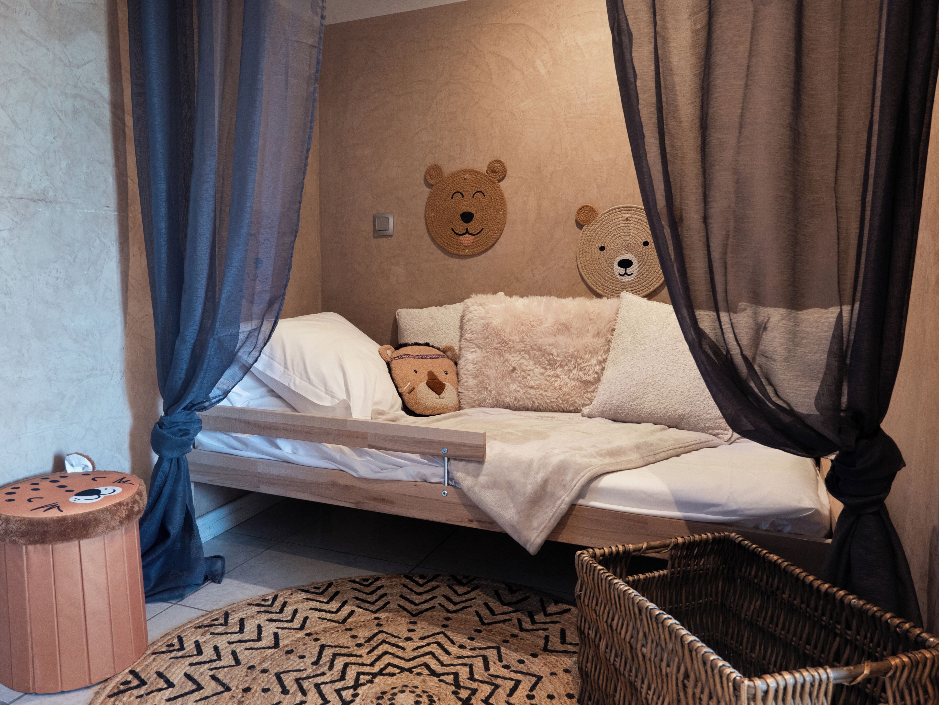 A cozy room with a bed, a small round stool, a woven basket, and a wall with bear-themed decorations.