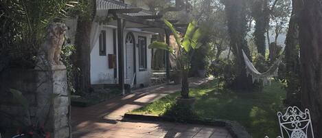 Un patio con suelo de baldosas, un edificio blanco con ventanas arqueadas y una hamaca.