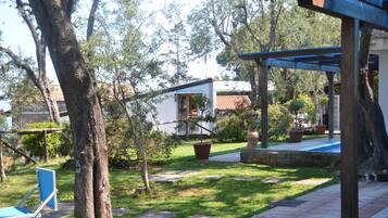 Um jardim com um edifício branco, uma cadeira azul e uma pérgola.