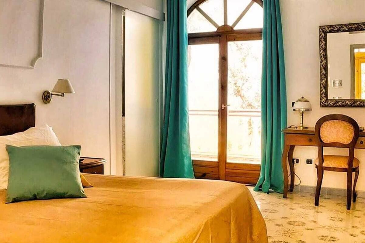 A hotel room with a bed, a desk, a chair, and a window with curtains.