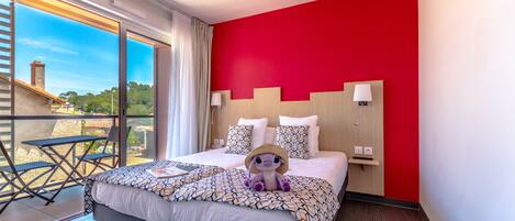 Habitación de hotel con una cama grande, vistas al exterior, una pared de acento roja y un balcón con mesa y sillas.