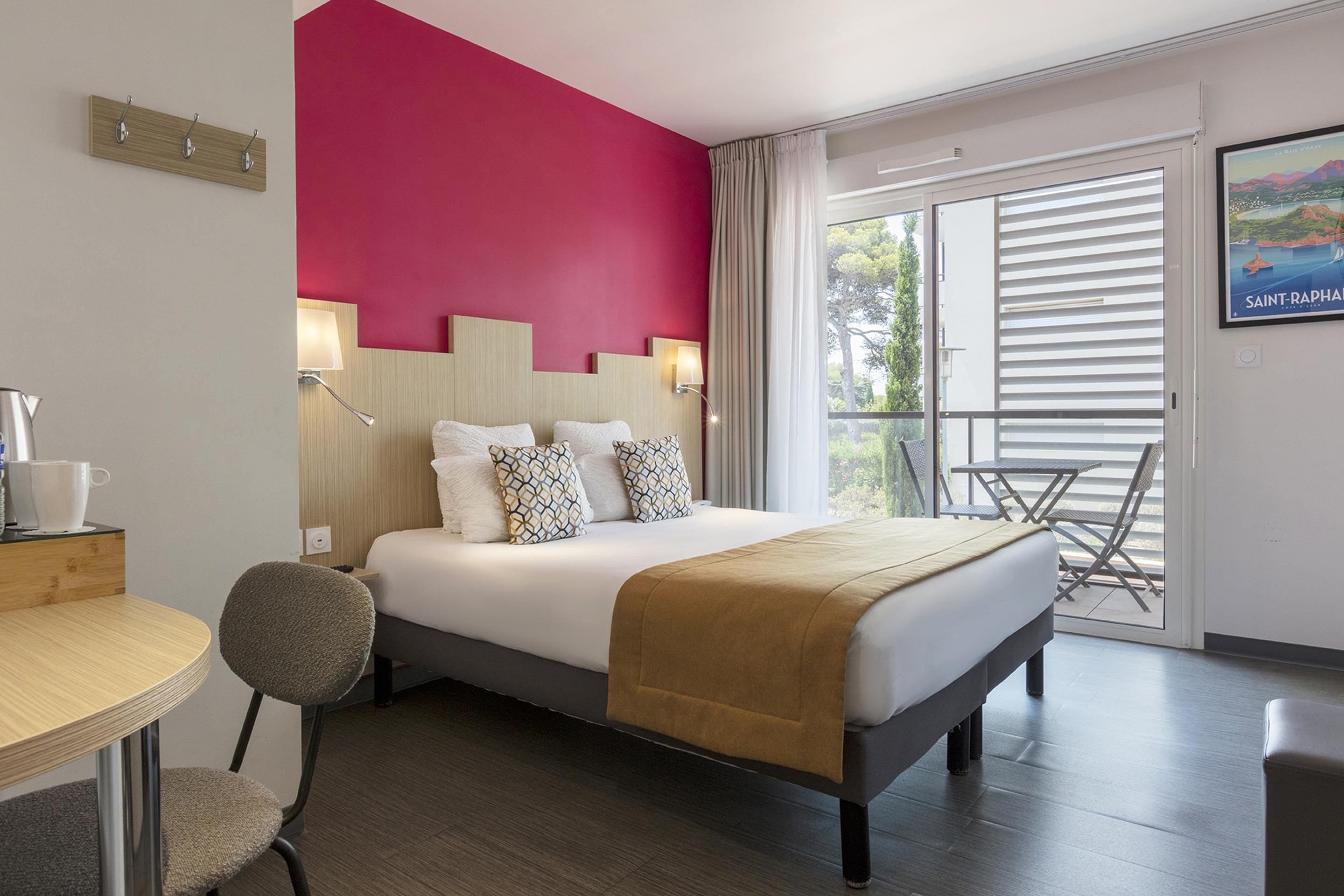 A hotel room with a bed, a desk, a chair, a balcony with a table, and a view of the outside.