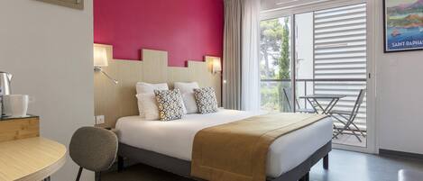 A hotel room with a bed, a desk, a chair, a balcony with a table, and a view of the outside.