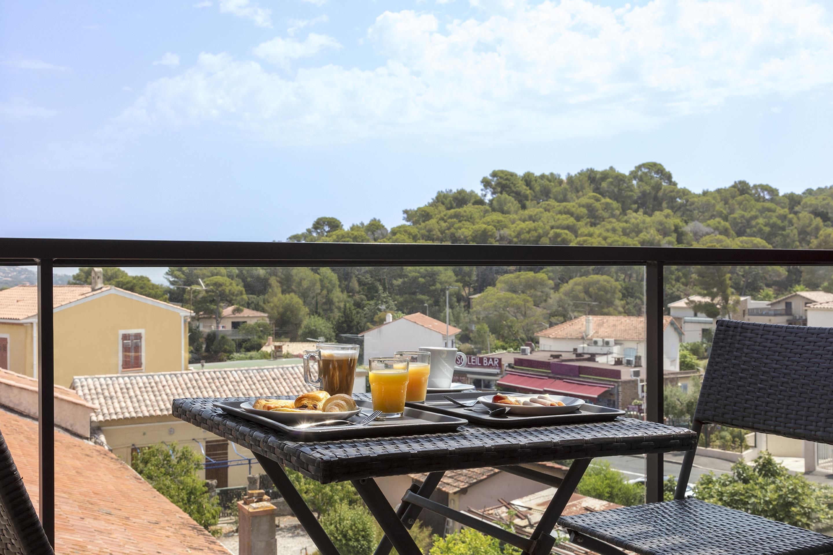 Een balkon met een ontbijttafel, met uitzicht op een woongebied met huizen en bomen.
