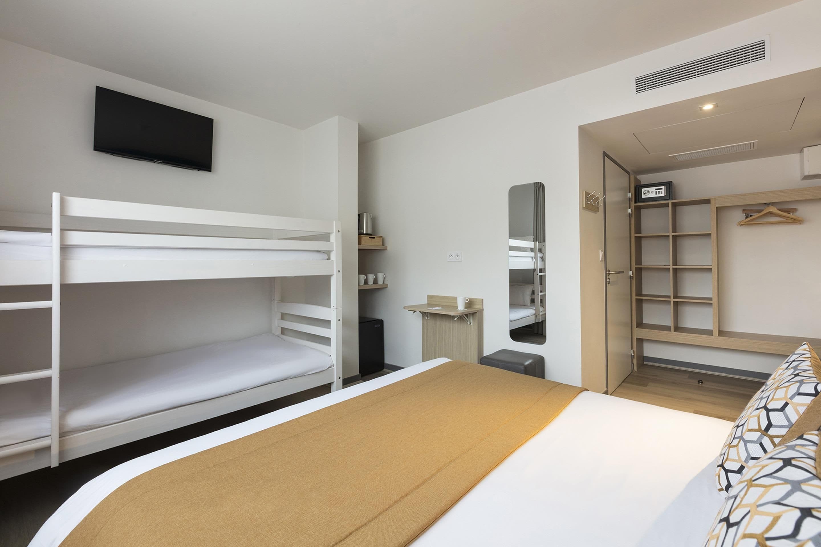 A hotel room with bunk beds, a television, a desk with a chair, a wardrobe, and a mirror.