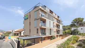 Un hôtel à plusieurs étages doté de balcons, d’un espace extérieur couvert aménagé en coin salon et d’un parking.