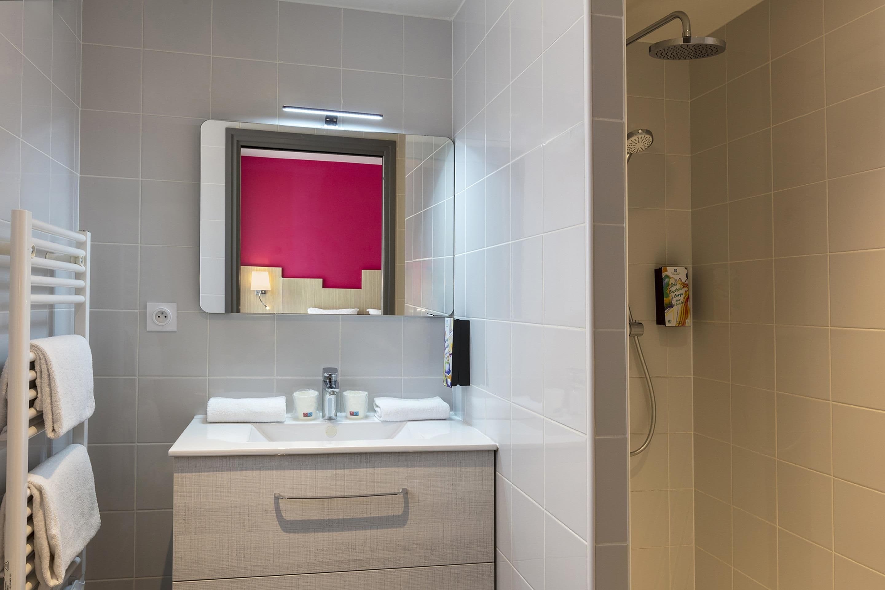 A modern bathroom with a white vanity, a mirror with a pink accent, and a shower area.