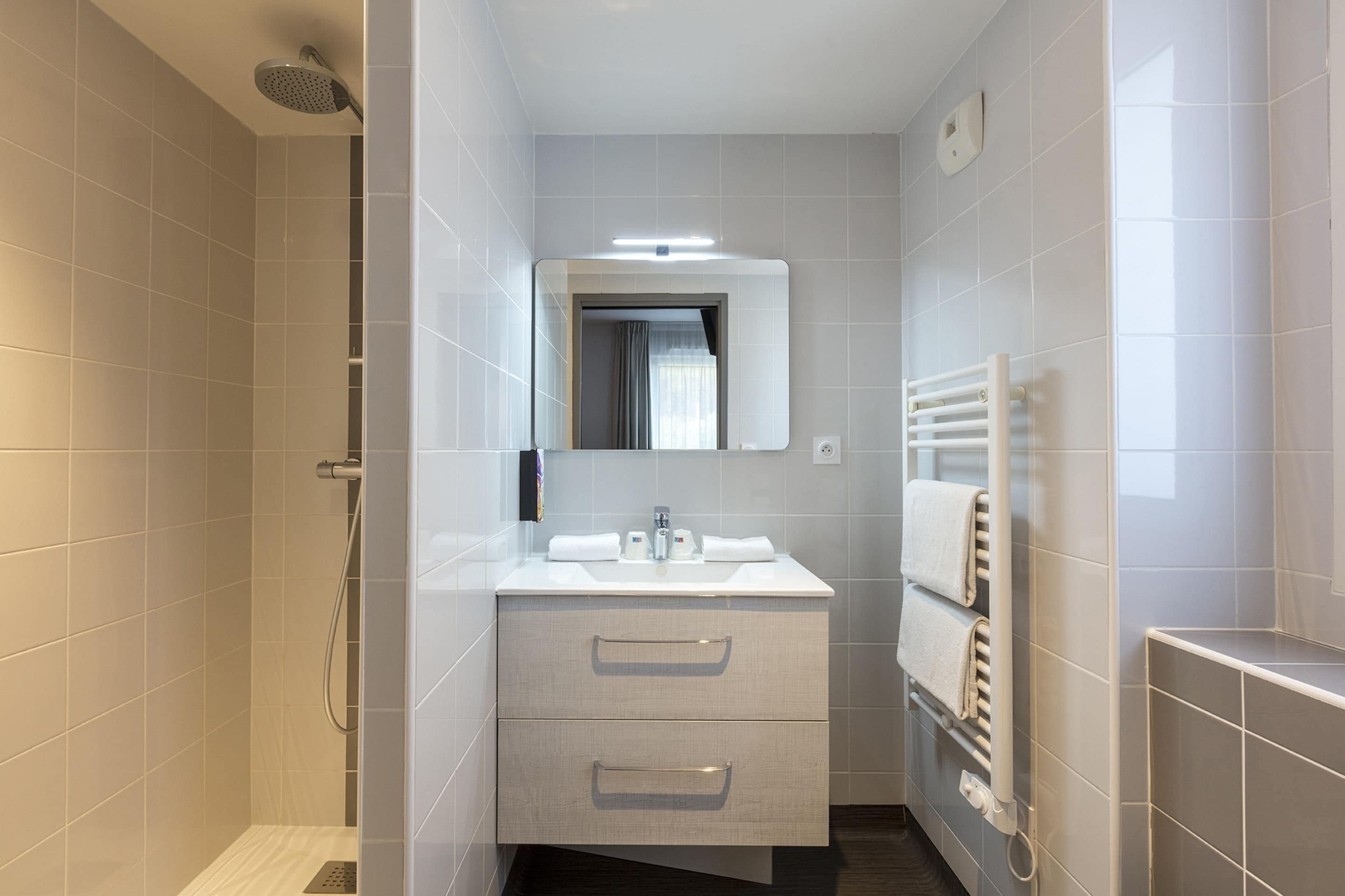 Une salle de bain moderne équipée d’une douche, d’un lavabo, d’un miroir et d’un porte-serviettes.