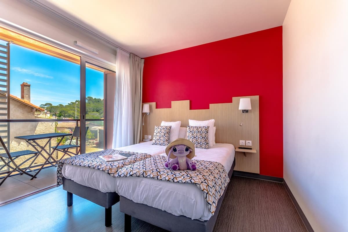 Habitación de hotel con una cama grande, un balcón con mesa y sillas, y una pared de acento roja.