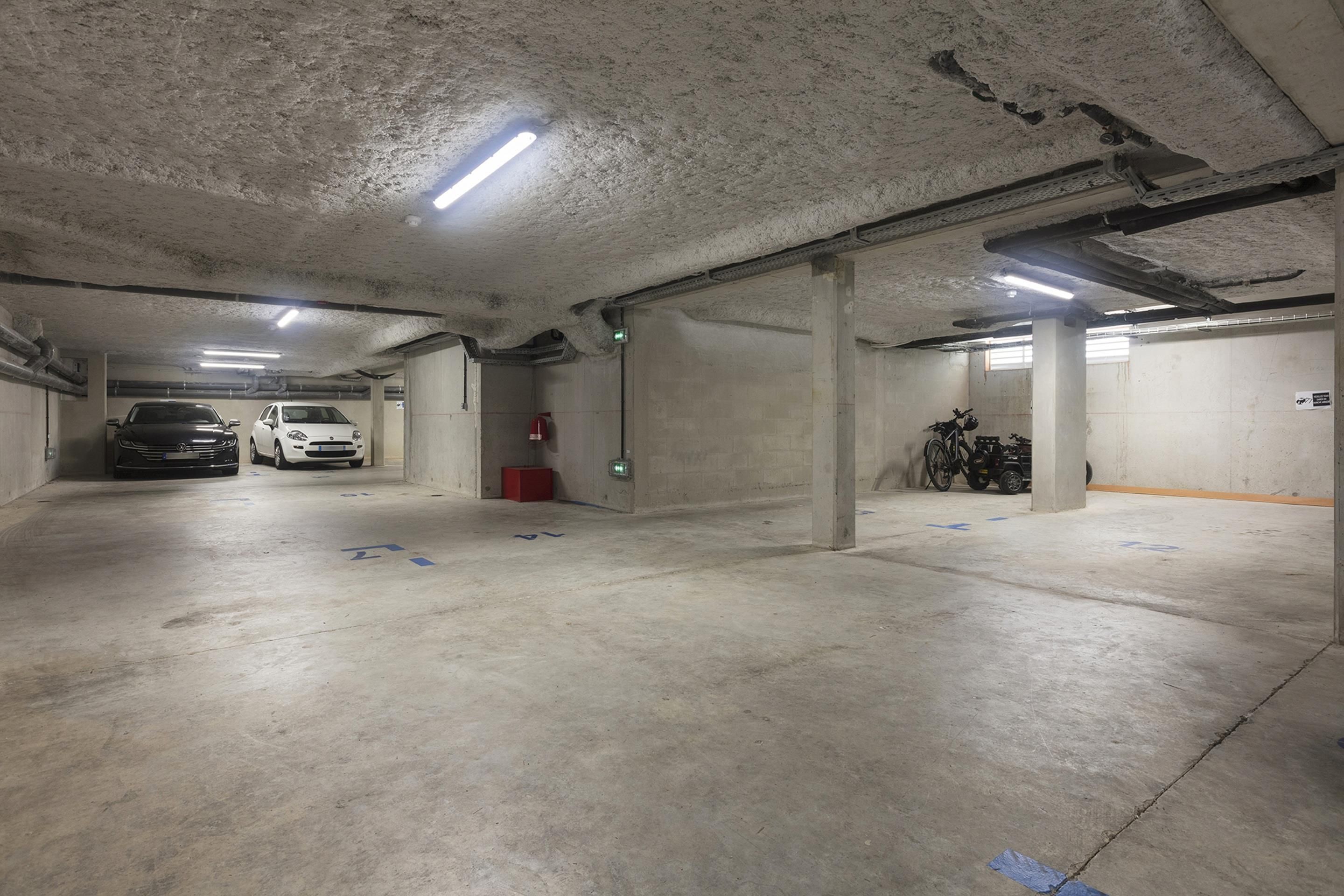 A parking garage with concrete pillars, fluorescent lighting, and marked parking spaces.