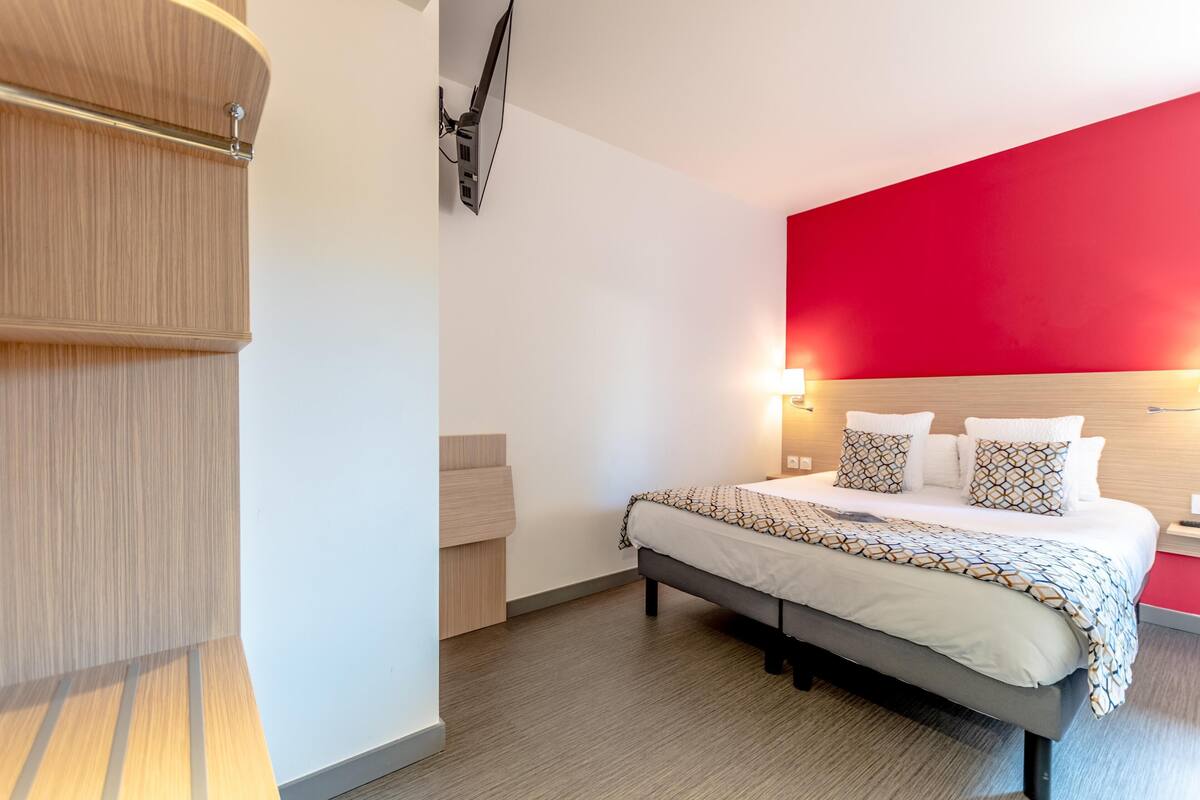 Una habitación de hotel moderna con cama, mesitas de noche, una pared de acento roja y un armario de madera.