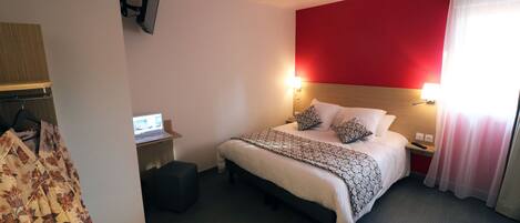 Habitació d'hotel amb un llit, taules de nit, un escriptori amb un ordinador i una televisió penjada a la paret.