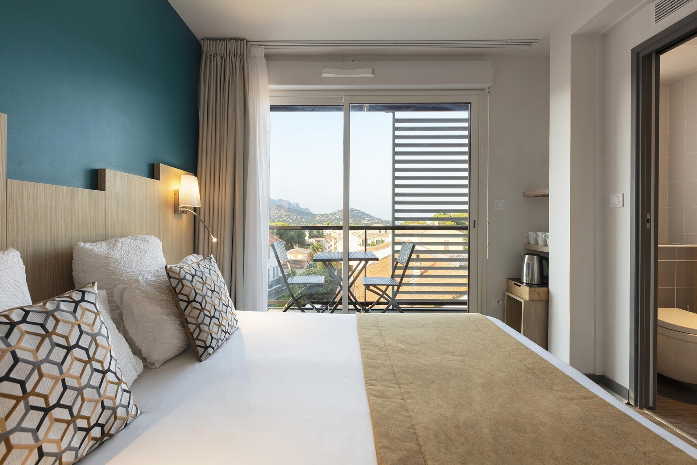 A hotel room with a bed, a desk, a chair, and a view of the cityscape.