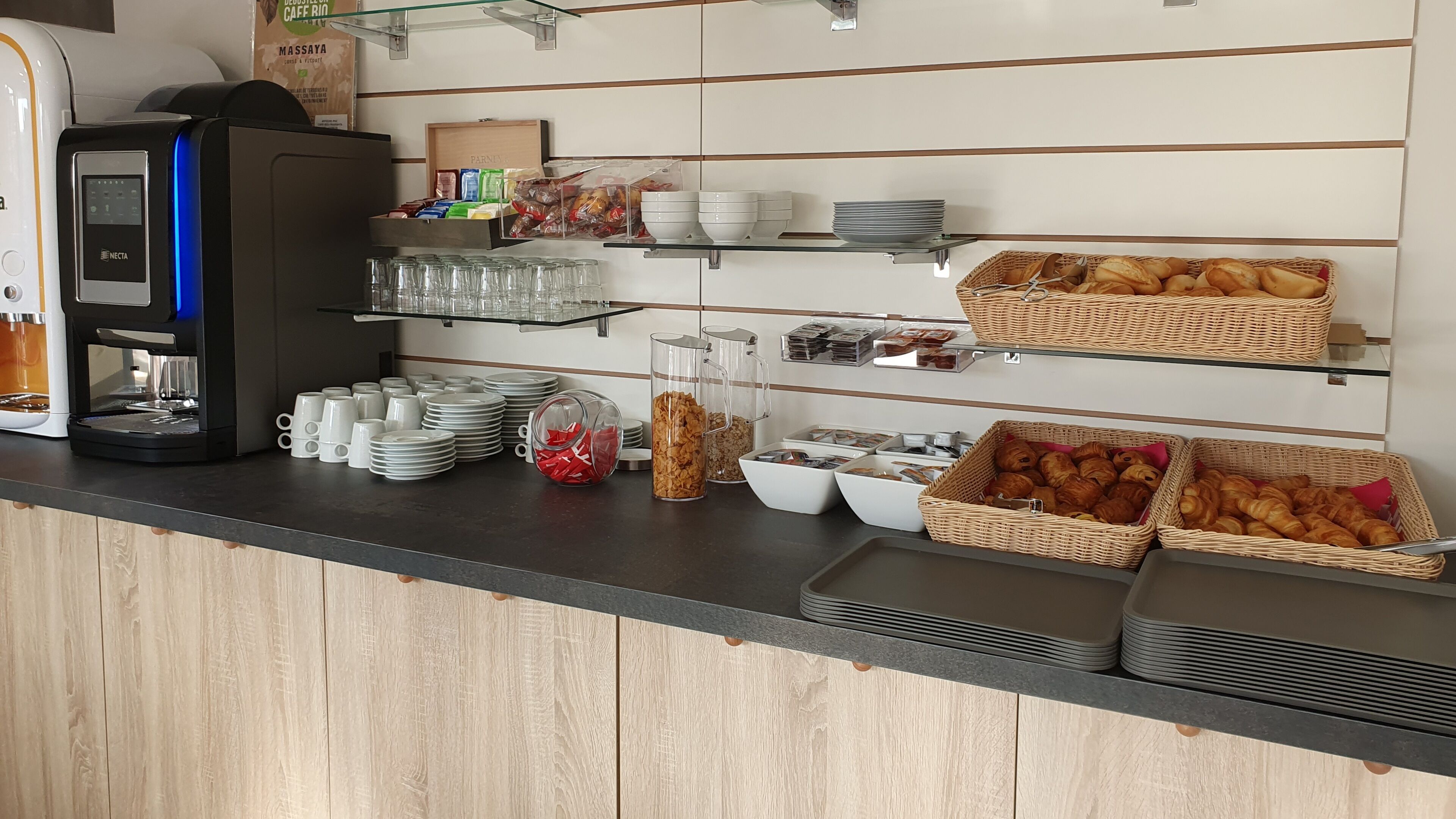 A breakfast bar with a coffee machine, stacked plates, bowls, and baskets of pastries.