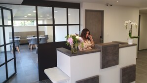A reception desk with a vase of flowers, a modern interior with a seating area visible through glass partitions, and a security camera on the ceiling. - Sure Hotel by Best Western Saint-Raphael Le Dramont (Saint-Raphael)
