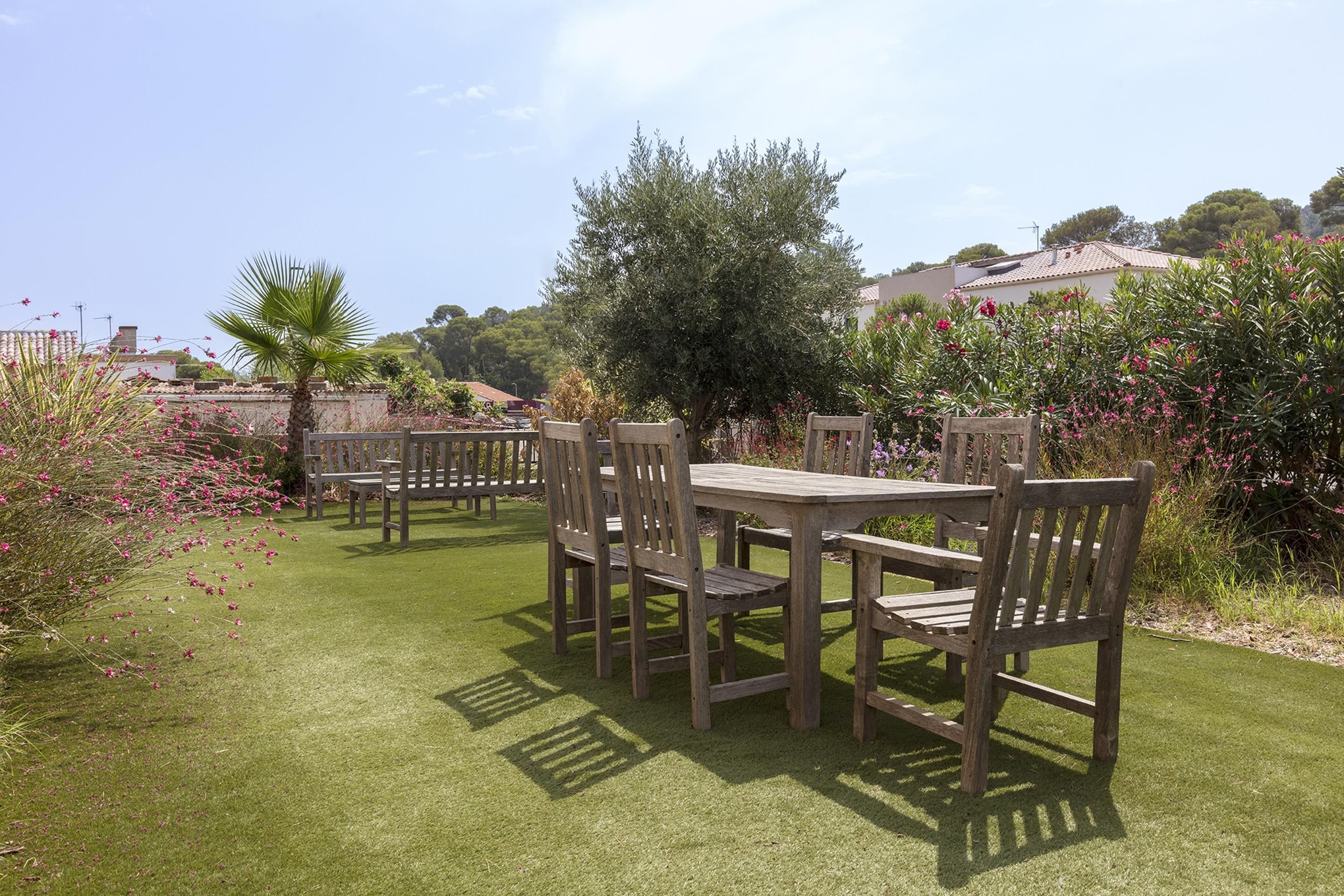 Un espace extérieur aménagé avec une table et des chaises en bois, entouré d’une pelouse bien entretenue et de diverses plantes.