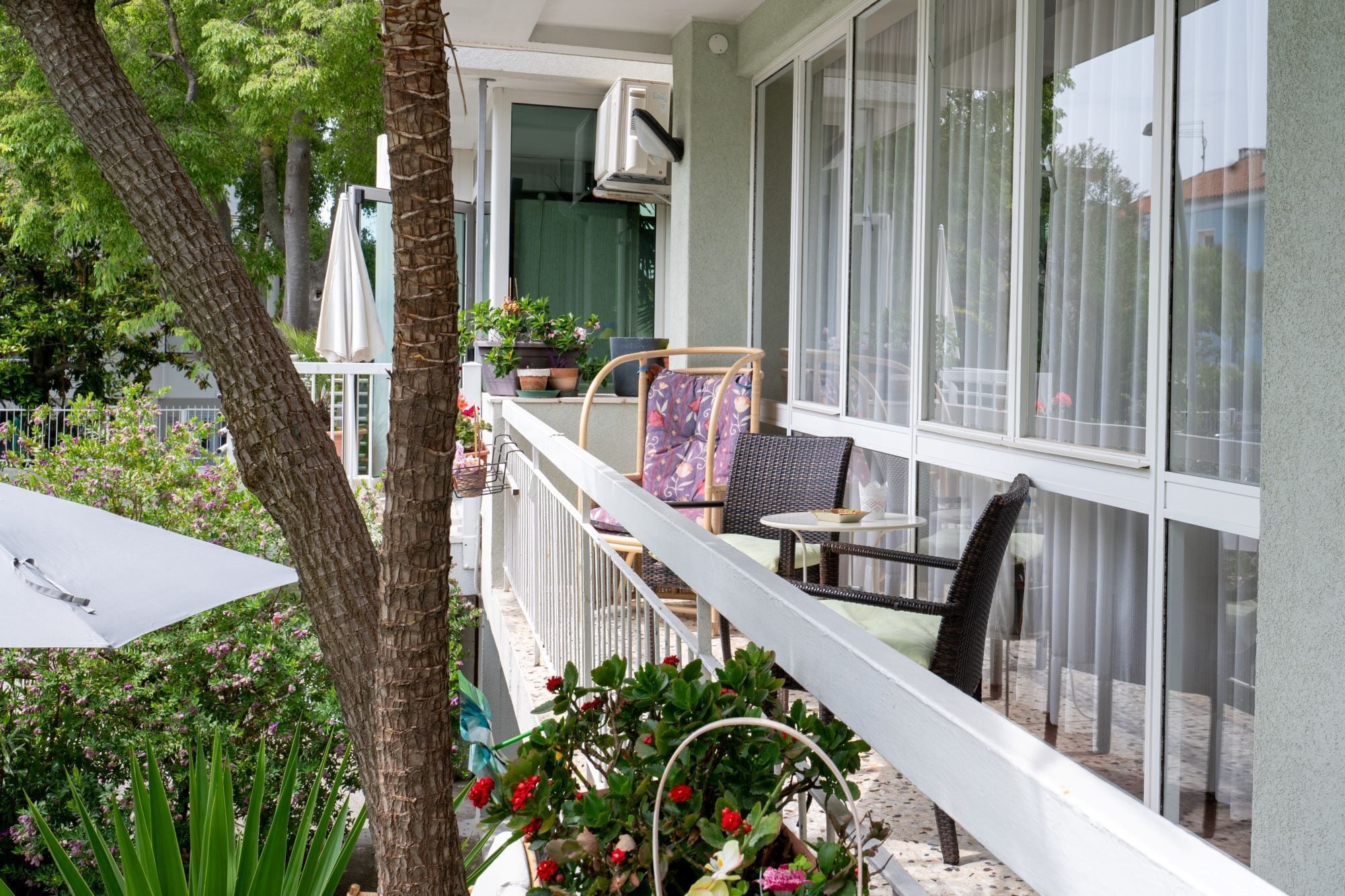A balcony with wicker furniture, potted plants, and a white umbrella.