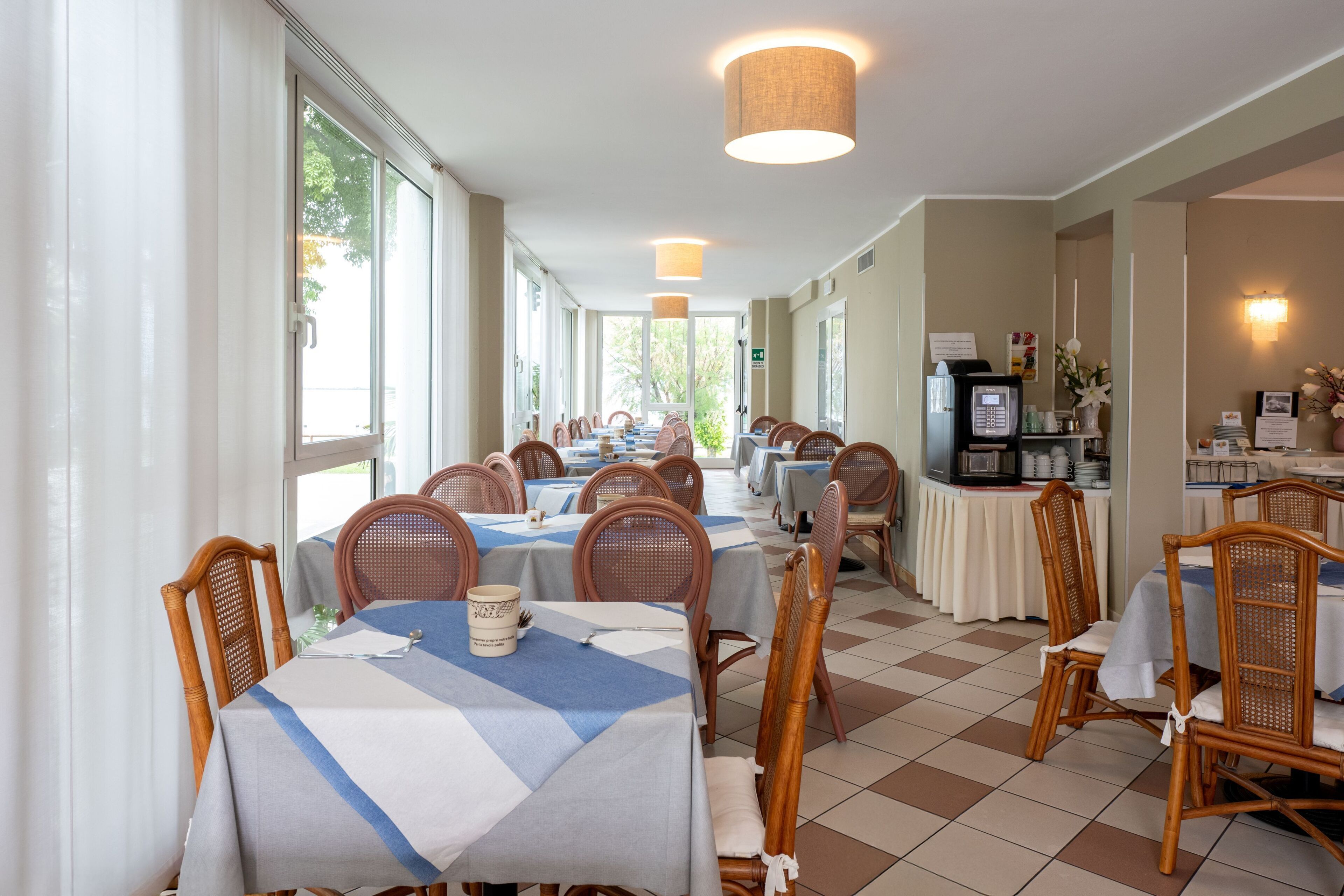 Un restaurante con varias mesas y sillas, amplias ventanas y una cocina visible al fondo.