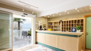 A reception area with a view of the sea, a reception desk, a welcome sign, and a small plant. - Capri (Grado)