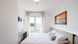 A bedroom with a bed, a painting of a sunset, a window with curtains, and a view of the sea. - Capri (Grado)