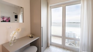 A modern hotel room with a large window, a vanity with a mirror, and a view of the sea. - Capri (Grado)