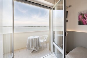 A balcony with a glass door, a small table with a striped tablecloth, and a white chair. - Capri (Grado)