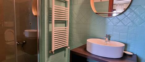 A bathroom with a glass shower enclosure, a white sink with a wooden vanity, and a mirror with a round frame.