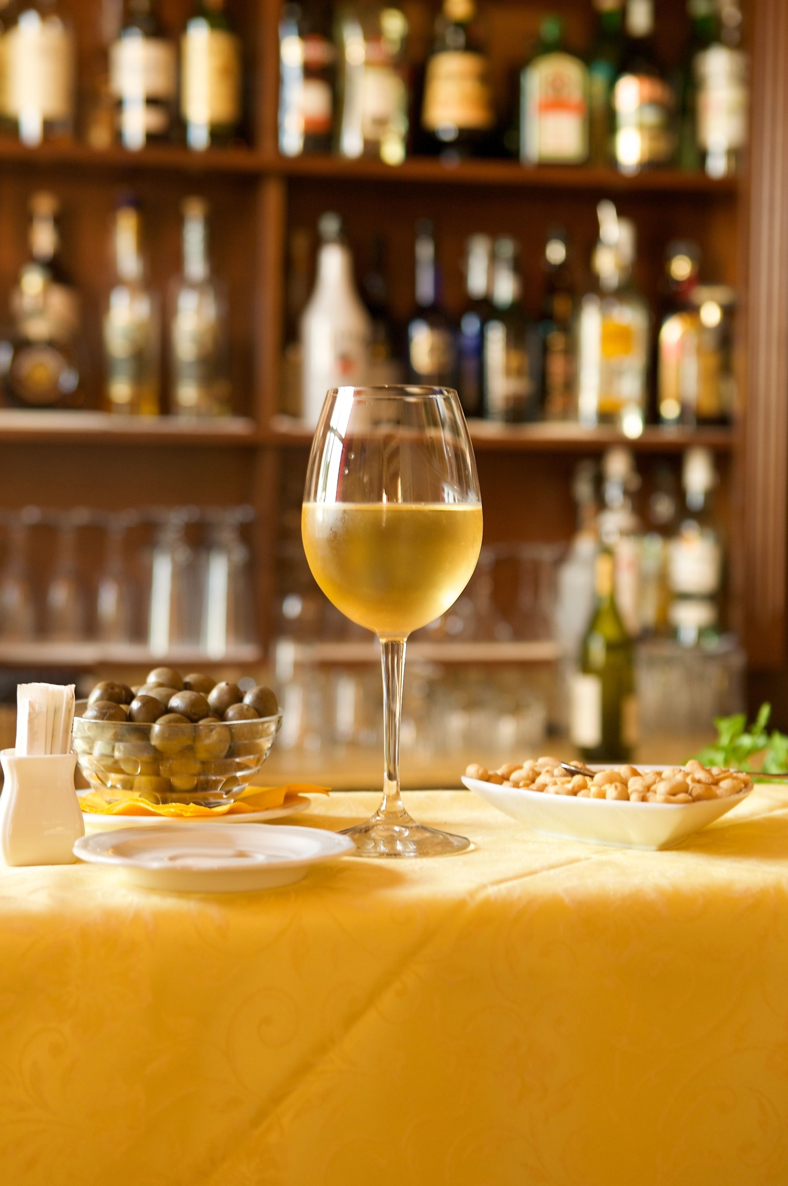 Un bar con un bicchiere di vino bianco, olive e arachidi su un tavolo.