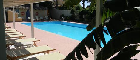 Zona de piscina con sillones de descanso y un flotador en la pared.