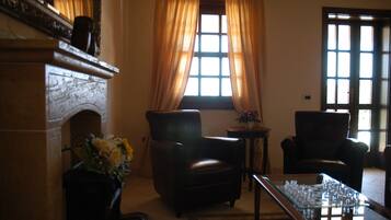 A room with a fireplace, two leather chairs, a coffee table, and a window with curtains.