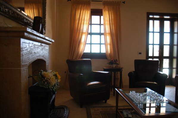 A room with a fireplace, two leather chairs, a coffee table, and a window with curtains. - Is Benas Country Lodge (San Vero Milis)
