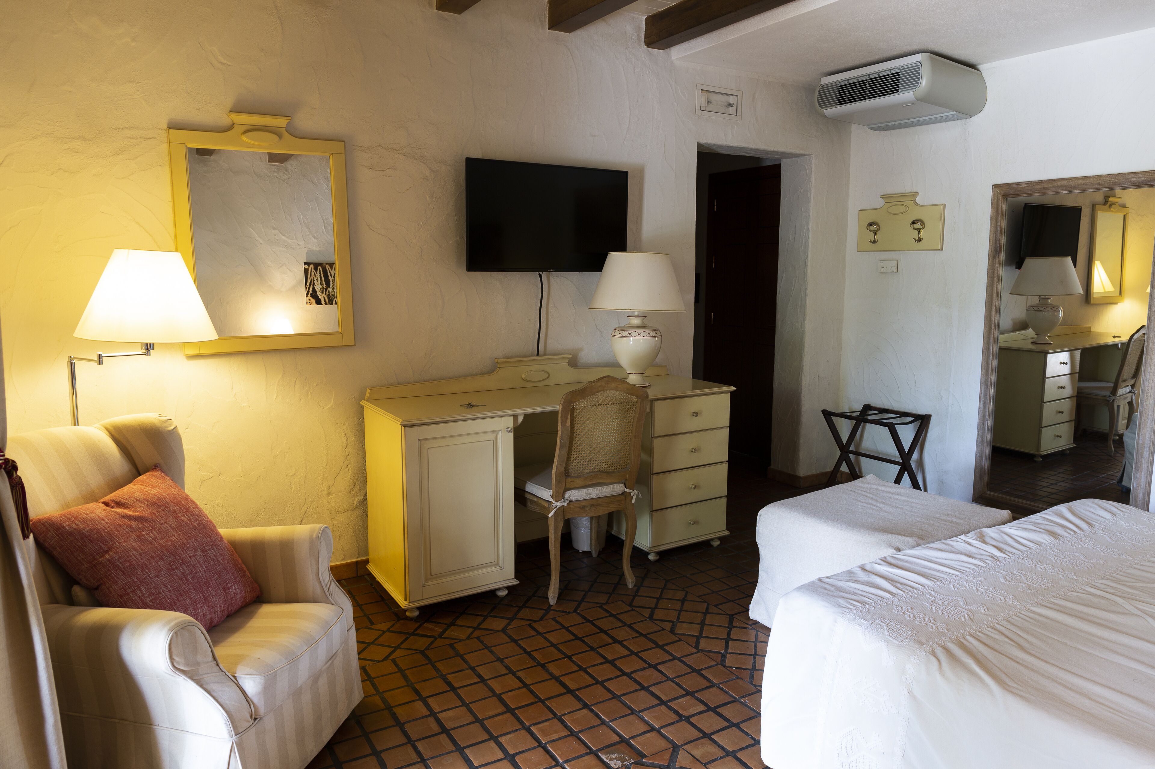 A hotel room with a bed, a desk, a chair, a television, and a mirror.