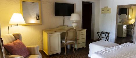 Una habitación de hotel con cama, escritorio, silla, televisor y espejo.