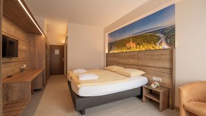 Een moderne slaapkamer met een groot bed, een houten hoofdbord, een nachtkastje, een stoel en een schilderij van een landschap aan de muur.