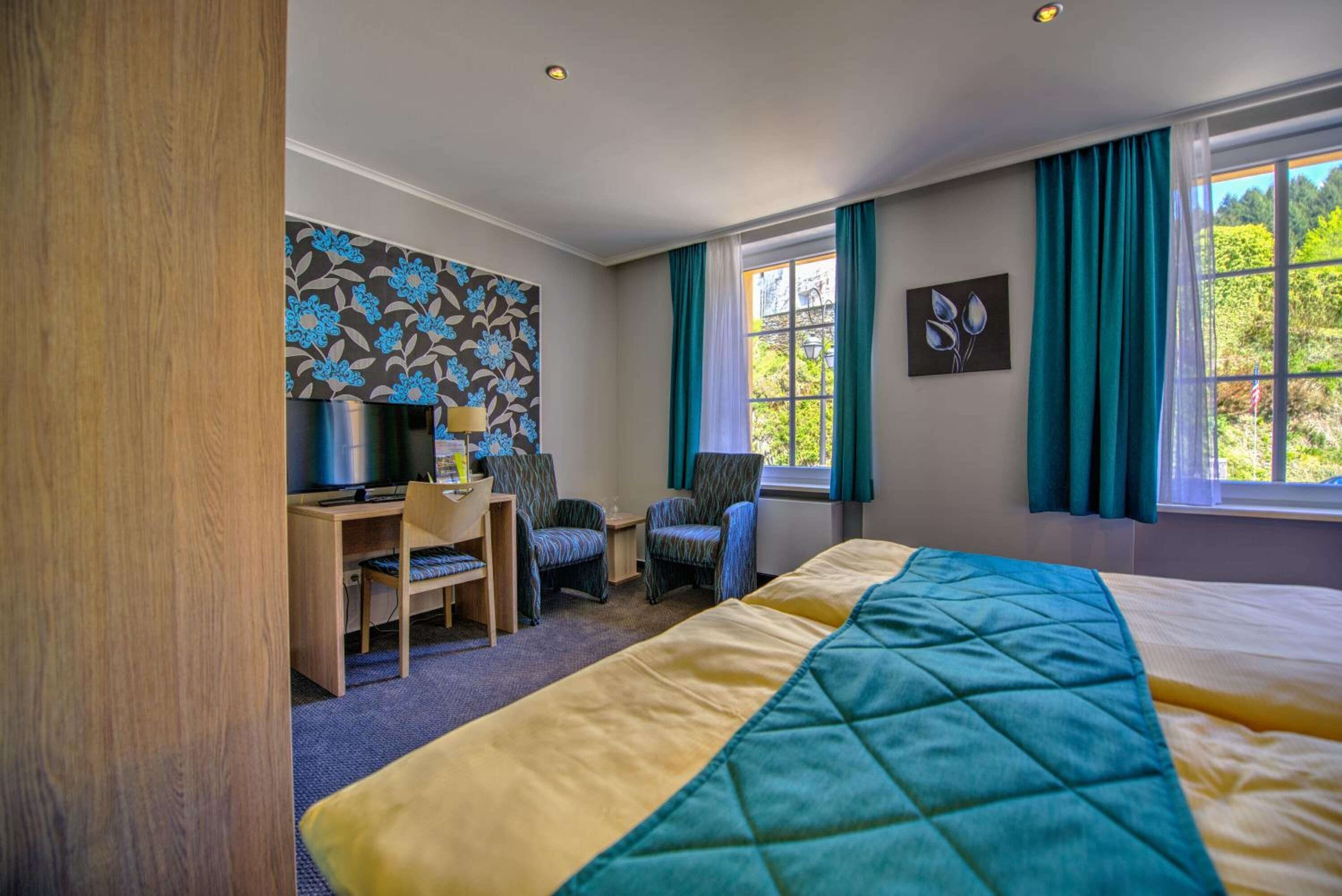 Habitación de hotel con cama, escritorio, sillas, televisor y ventana con cortinas.