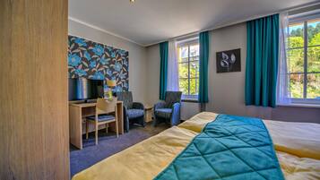 Habitación de hotel con cama, escritorio, sillas, televisor y ventana con cortinas.