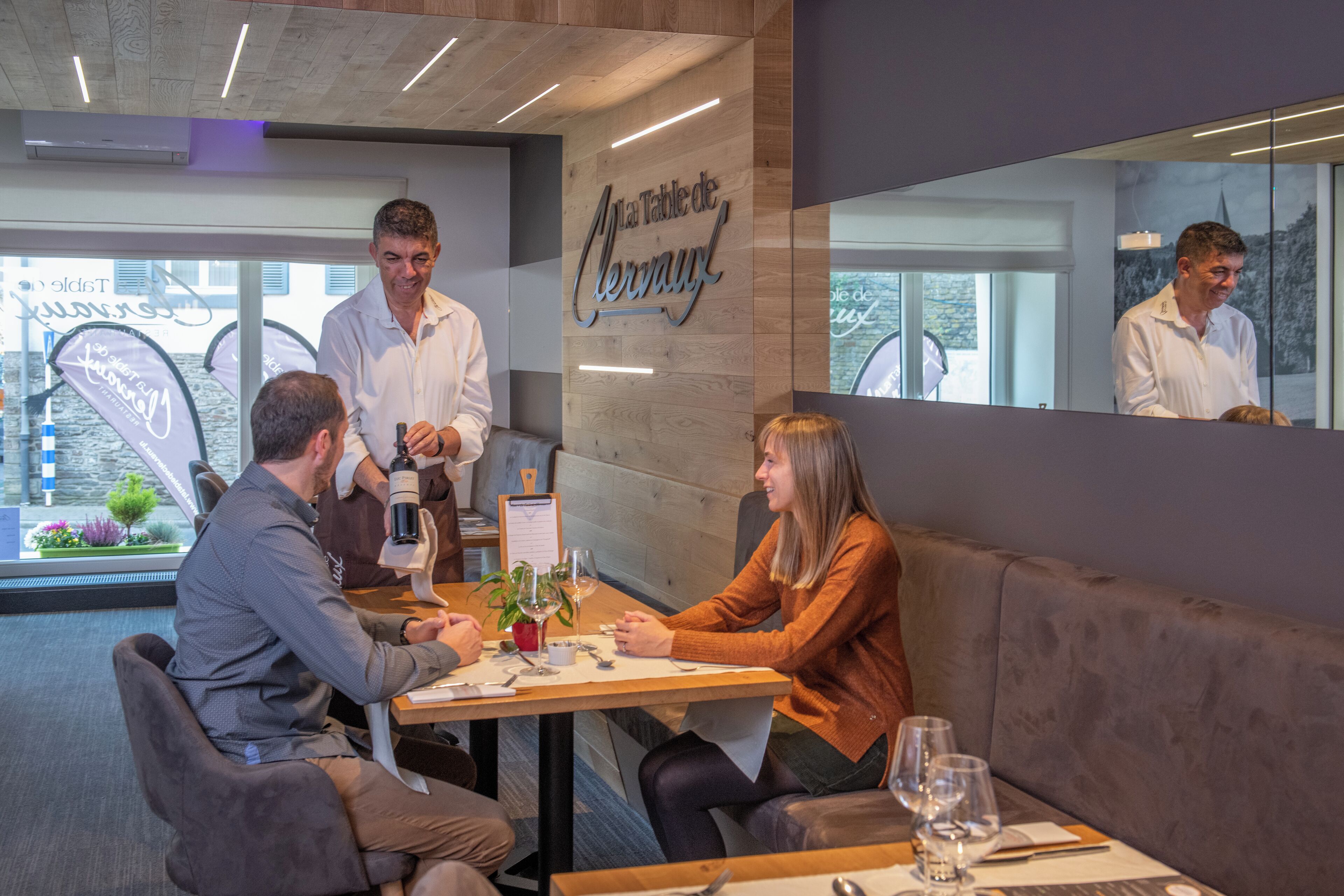 Un interior de restaurante con una mesa de madera, un menú y una copa de vino sobre la mesa.