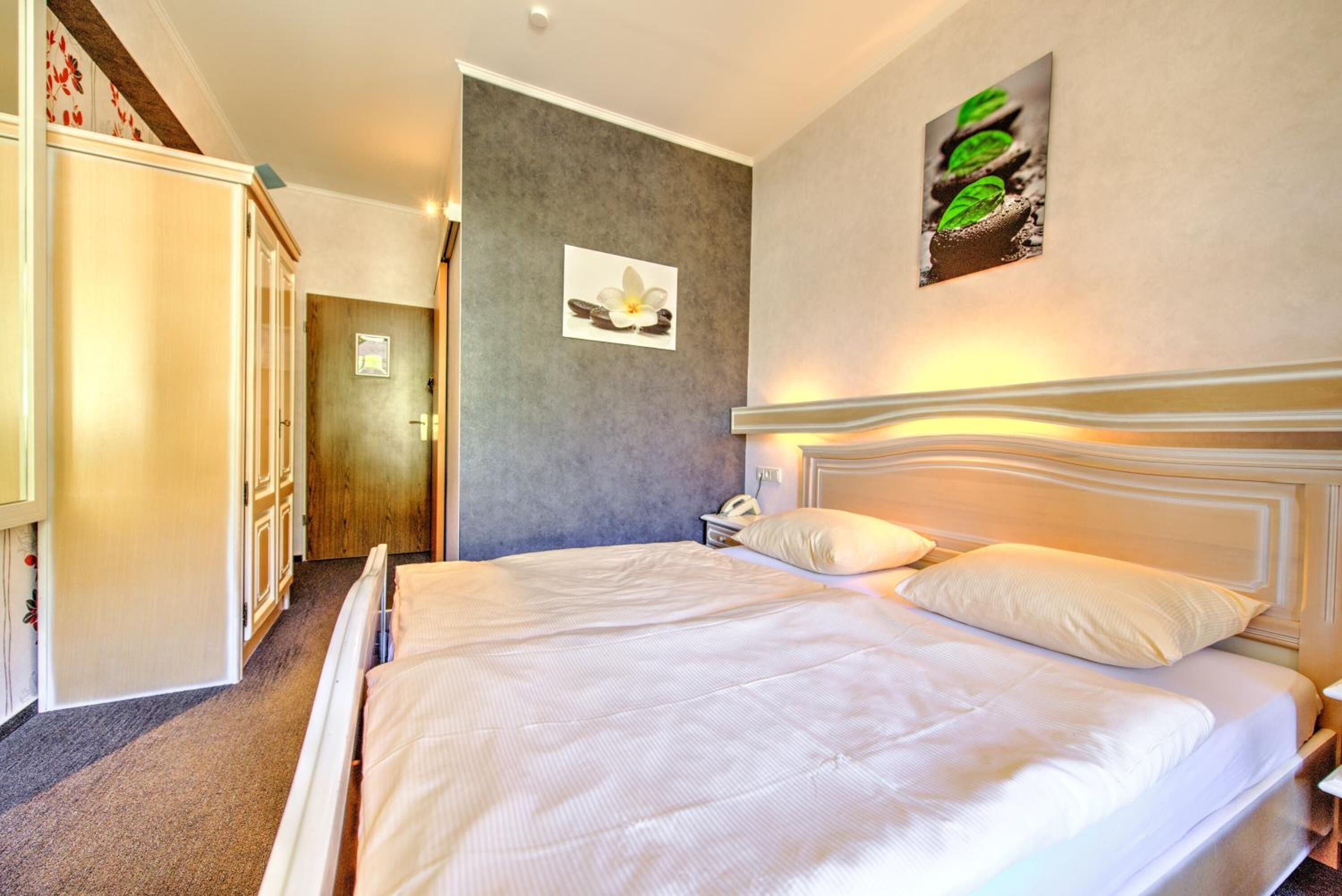 Une chambre d’hôtel avec un grand lit, une armoire, une porte et un mur orné d’un tableau.
